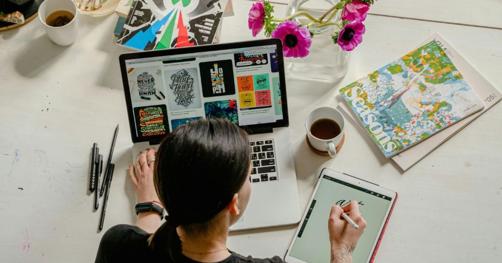 Creative woman working at a desk with a laptop, tablet, and art supplies