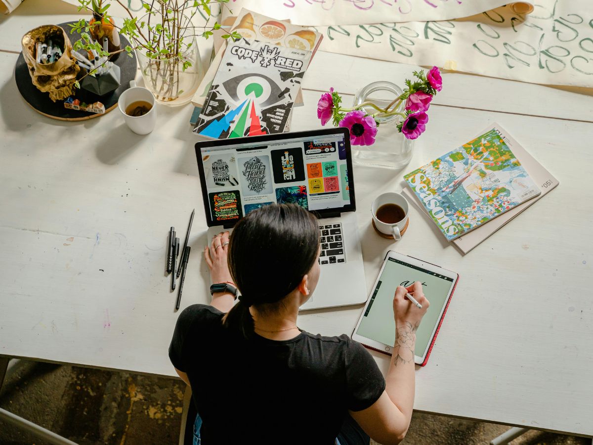 Creative woman working at a desk with a laptop, tablet, and art supplies