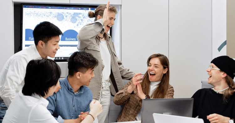 Work team crowded around a laptop celebrating. Office setting.