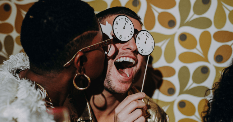 Man and woman at party. Man wearing countdown clock mask. Woman kissing man's cheek